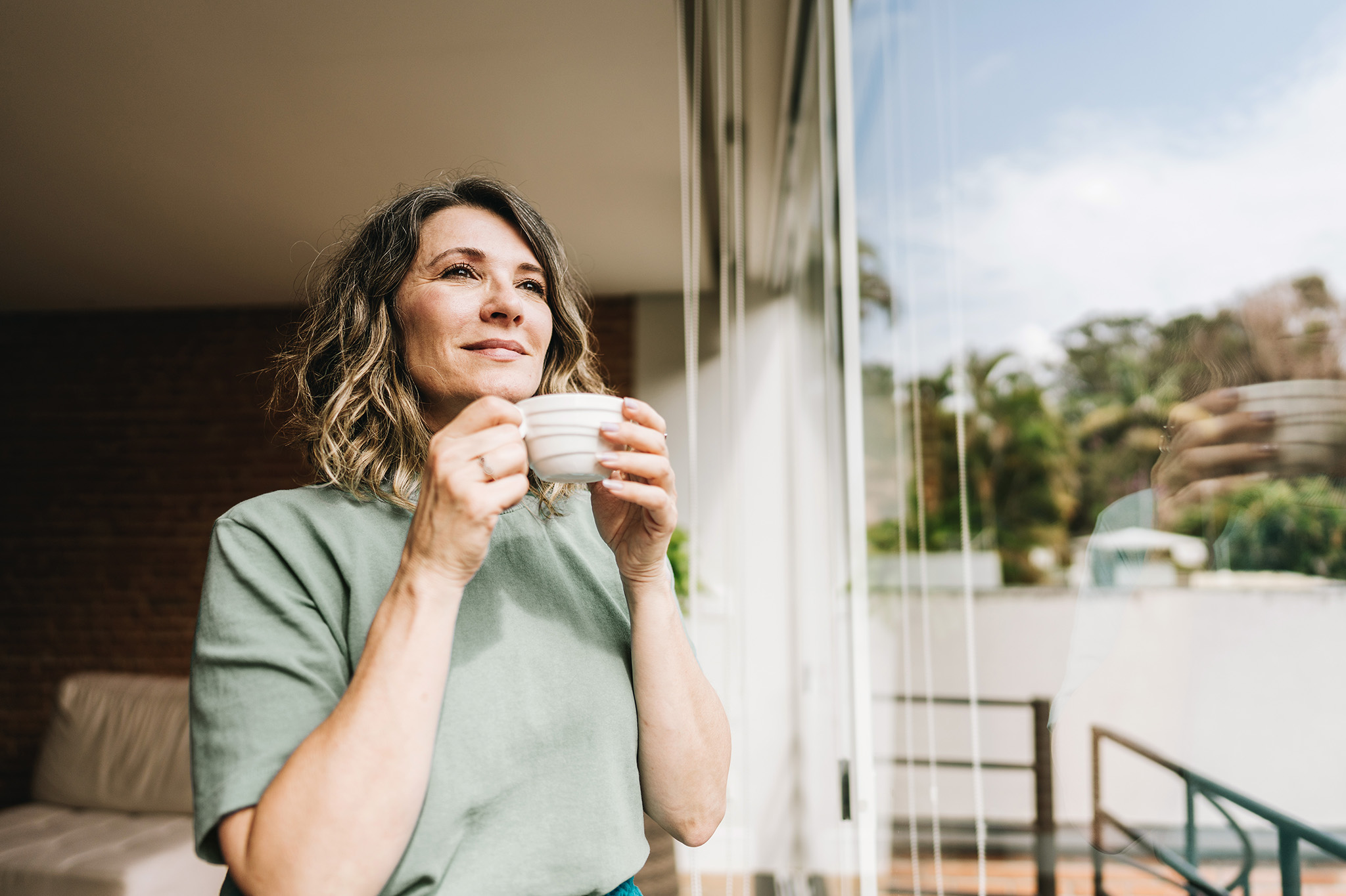 Contemplative mature woman looking throught the window at home